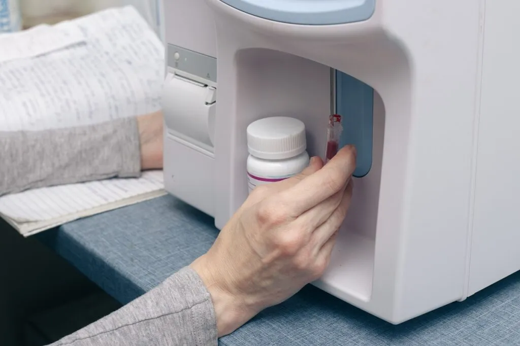 Une main place un échantillon de sang dans une machine pour l'analyser