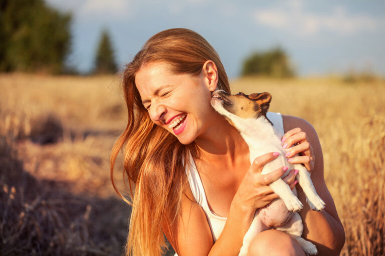 Junge Frau hält Jack Russel in ihren Händen, während der Hund die Frau im Gesicht abschleckt